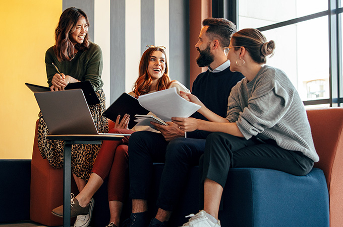 Cuatro emprendedores, tres mujeres y un hombre, sonrientes con papeles y laptop